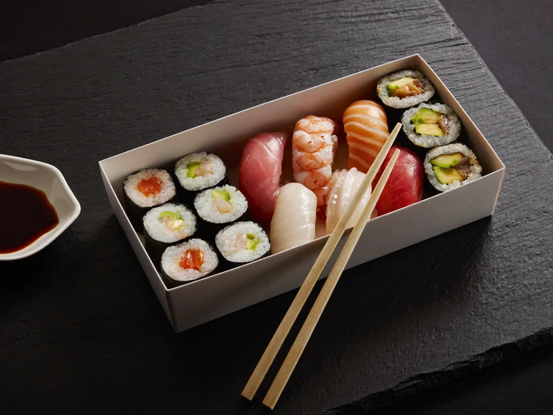Neutral sushiboks med rúller, nigiri og spisepinde på mørk skifer